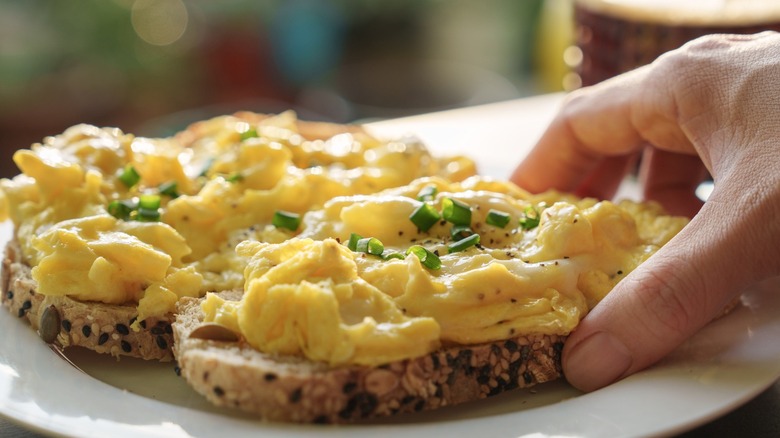 Hand reaches for fluffy scrambled eggs on toast
