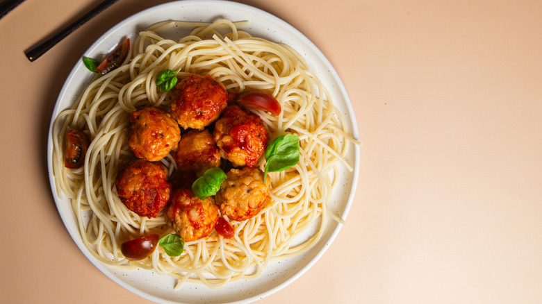 Spaghetti and meatballs with tomato sauce, basil and cherry tomatoes on a plate.