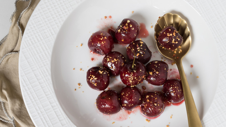 Cherries jubilee in close-up on a white plate with a bronze spoon.