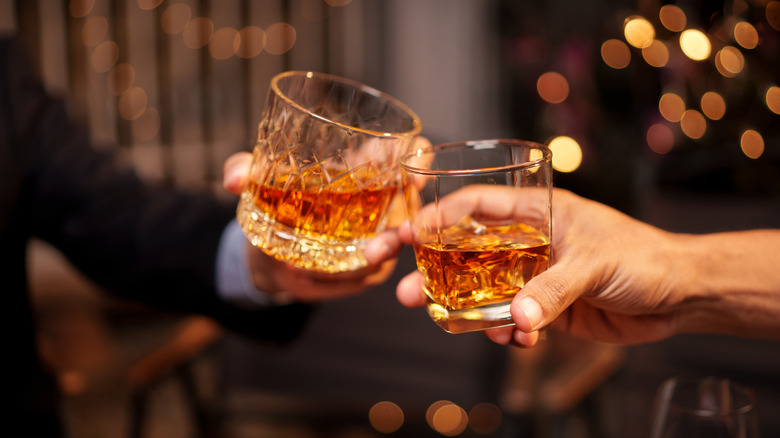 two people toasting with bourbon in glasses