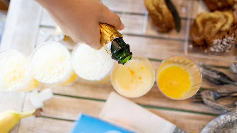 Tangan menuangkan sampanye ke dalam jus jeruk untuk mimosa