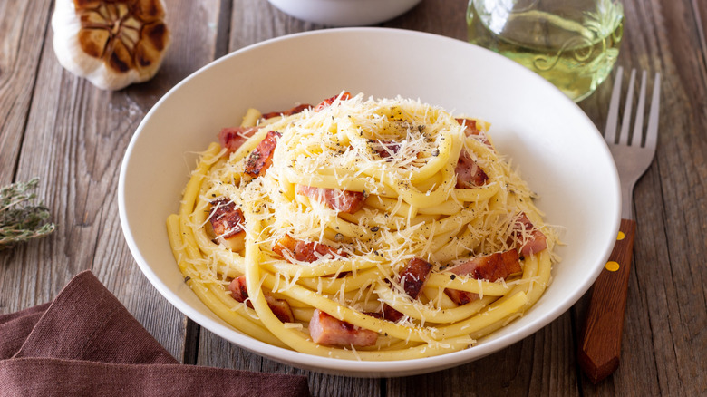 A bowl of bucatini carbonara on a wooden table.