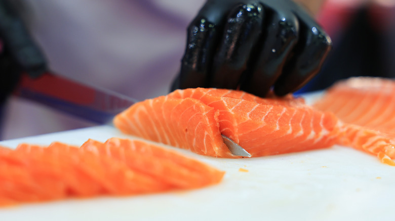 Gloved hands slicing raw salmon