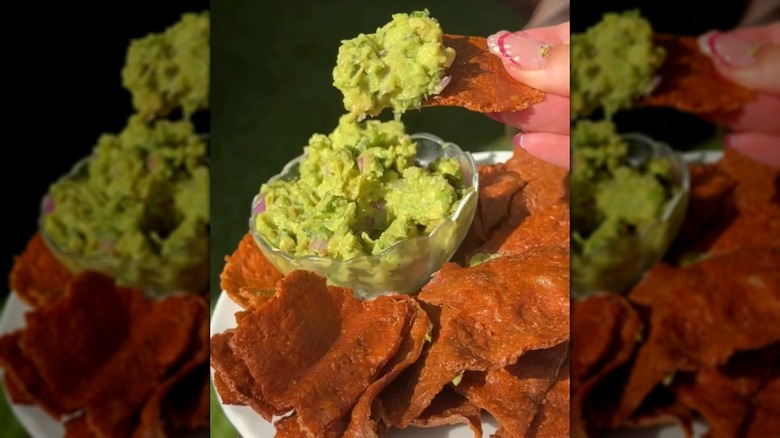 Hand dipping chicken chips into a side of guacamole