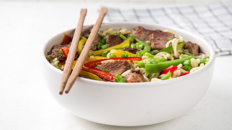 bowl filled with beef lo mein noodles and a pair of chopsticks