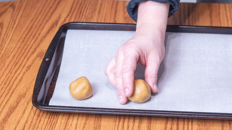 peanut butter balls being placed on a cookie sheet