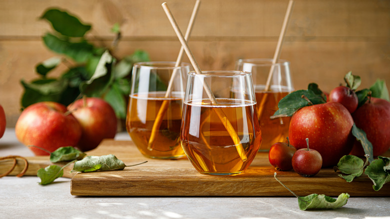 Two glasses of apple juice on a wooden surface next to whole apples