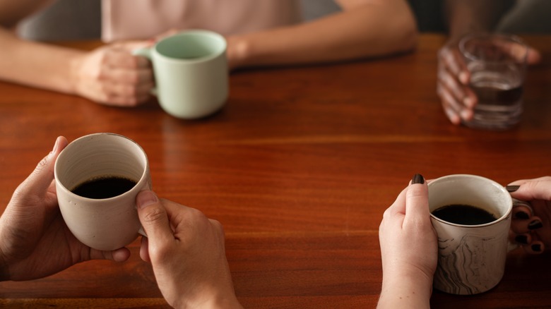 A group of people gathered at a table drinking cups of coffee.