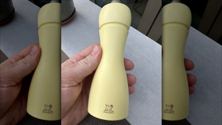 Person's hand holding a yellow Peugeot pepper grinder