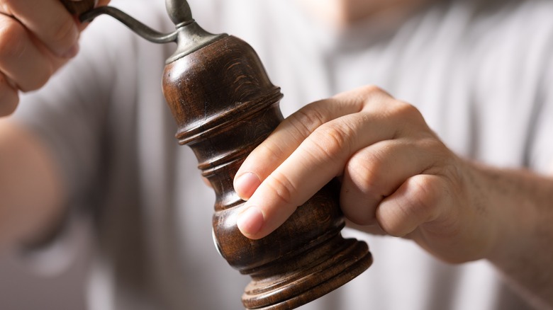 A hand operating an antique pepper grinder.