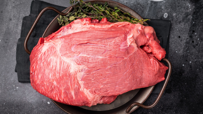 Raw top round roast cut of beef in deep pot on counter.