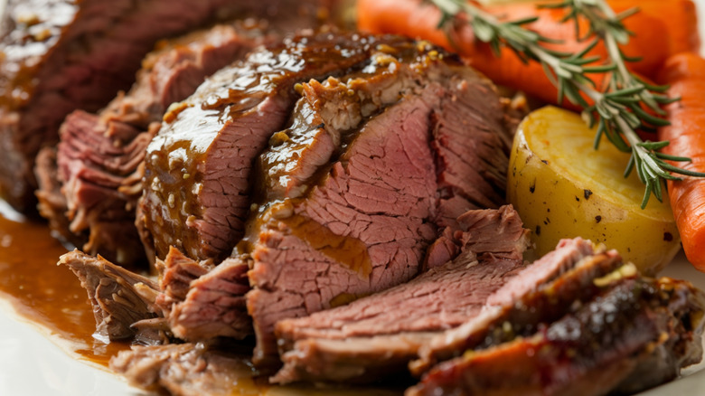 Cooked sliced pot roast with carrots, potatoes, and rosemary sprigs.