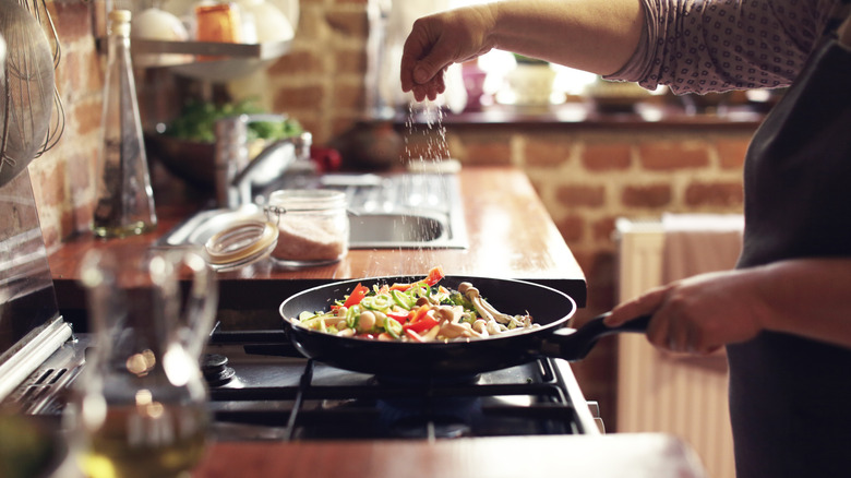 Hand sprinkling salt over a pan of sautéing vegetables
