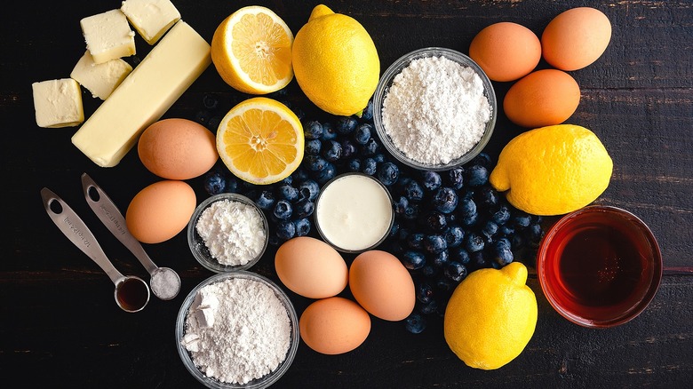 Blueberries, lemons, brown eggs, butter, and bowls of powdered ingredients on a wooden surface