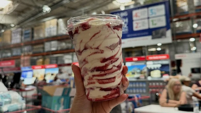 A person's hand is seen holding a white and purple swirled soft serve sundae at a Costco.