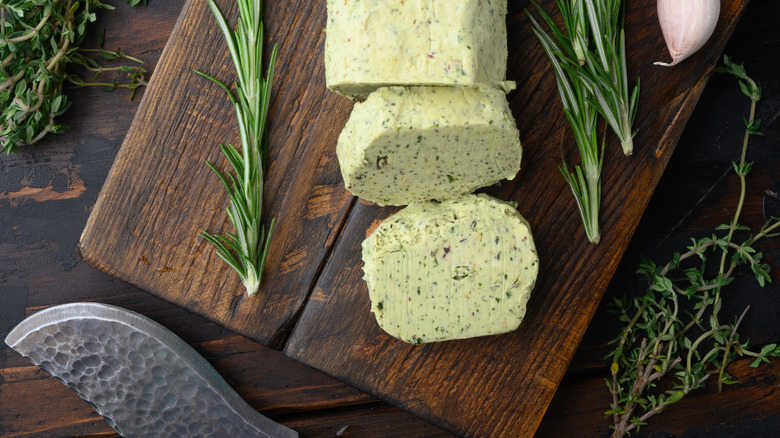compound butter on a wooden cutting board with fresh herbs on the side