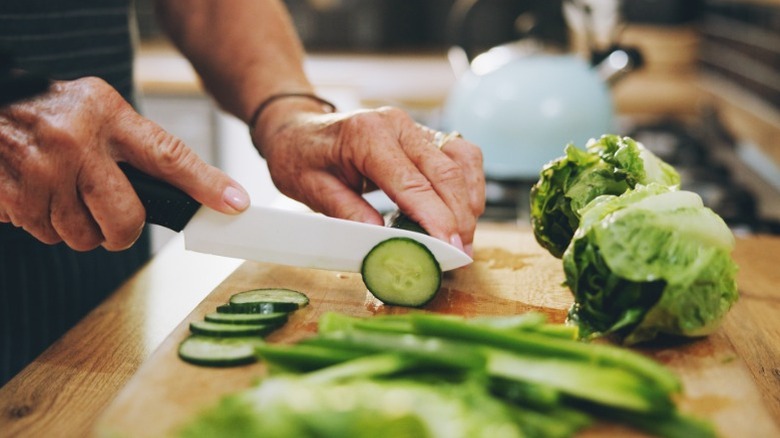 A person cutting cucumbers on a wooden cutting board in a kitchen.