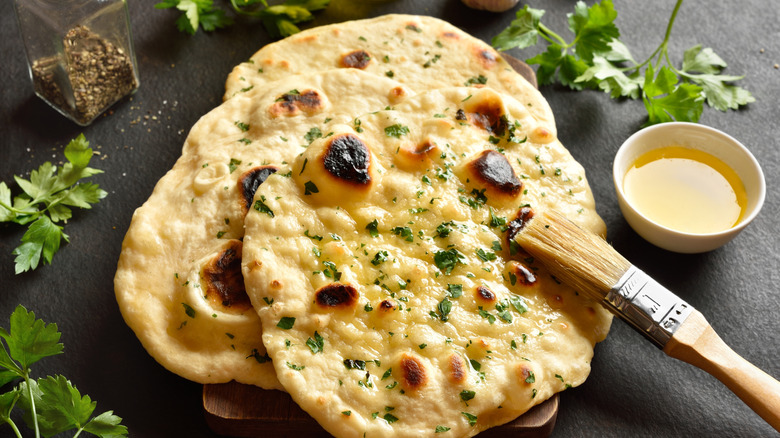 Butter being spread on naan bread with cilantro sprinkled on top.