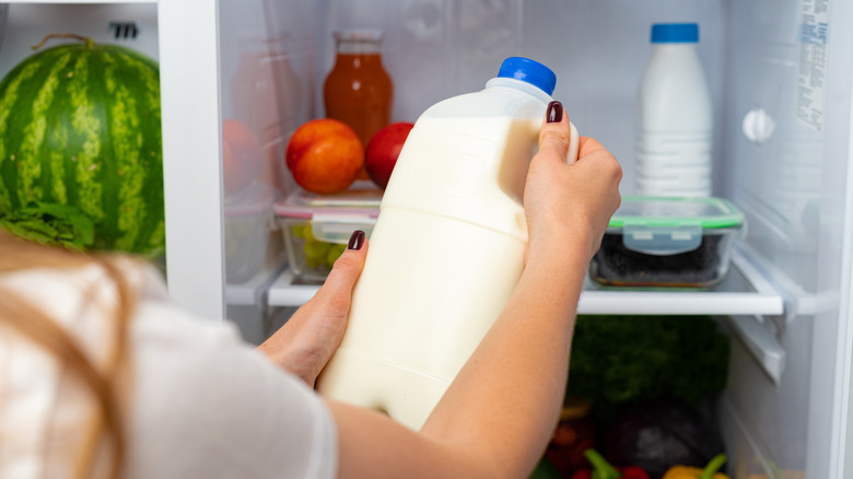 A person's hands are seen holding a container of milk in front of a refrigerator.