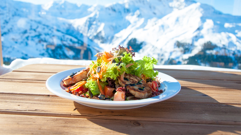 Salad in a white bowl on a wooden table with snowy mountains the background