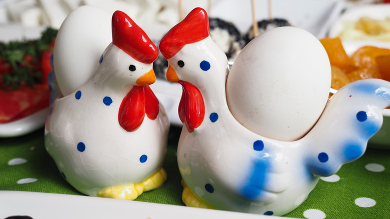two ceramic rooster egg holders next to each other on a green table