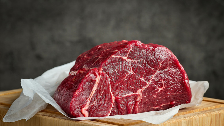 A huge chunk of raw meat on top of a wooden table