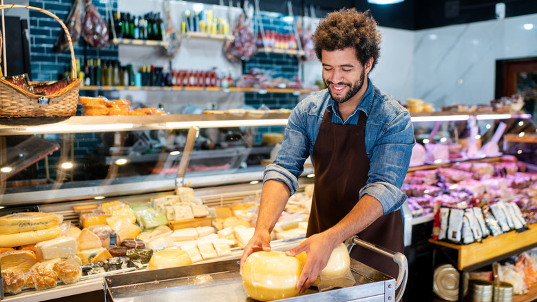 A deli worker moves a cart with cheese in front of deli counter