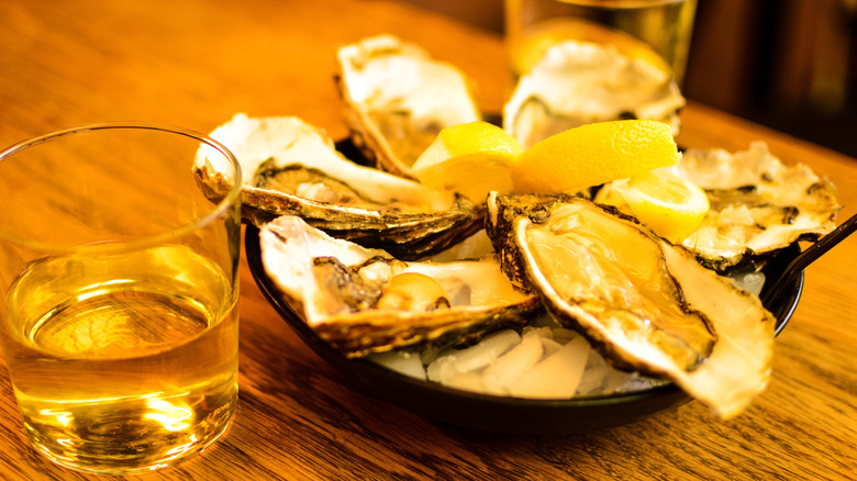 Oysters are with a glass of whiskey on a wooden table.