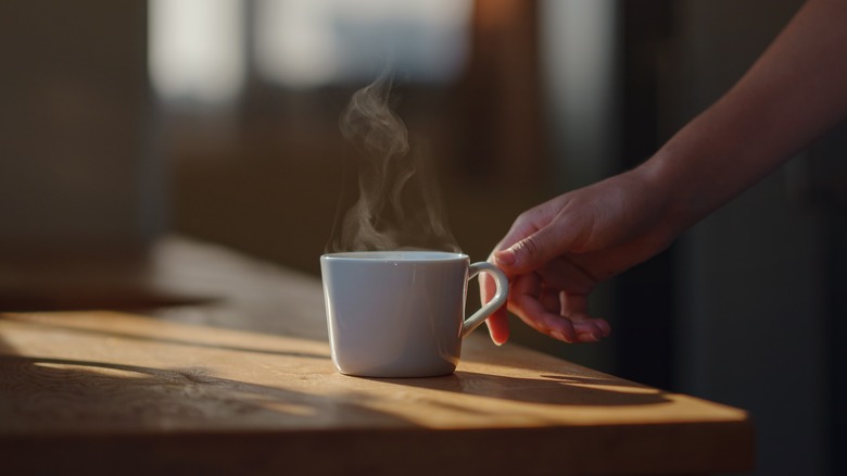 Hand reaching for steaming cup of coffee