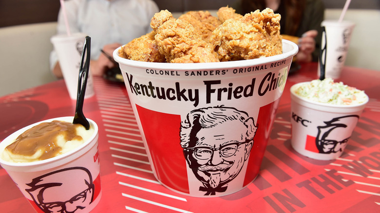 A KFC fried chicken bucket with coleslaw and mashed potatoes.