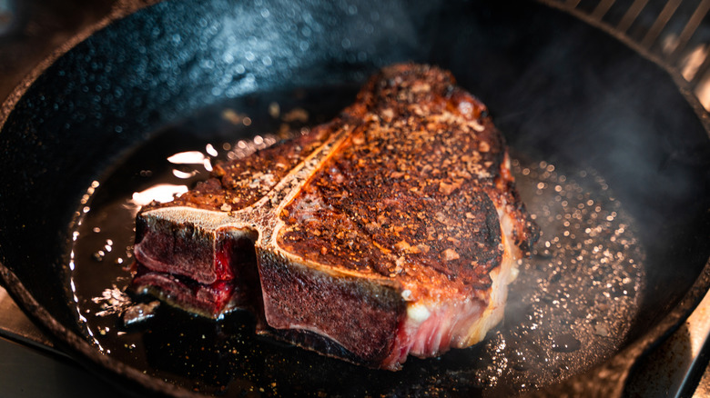 A t-bone steak searing inside a cast iron skillet