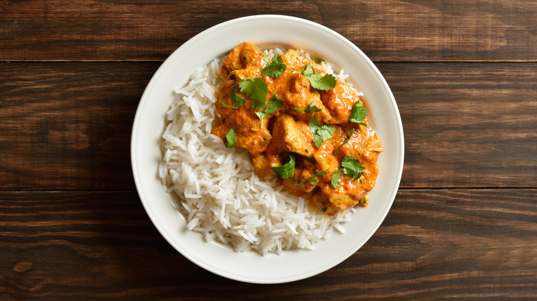 A plate of butter chicken with rice on the side.