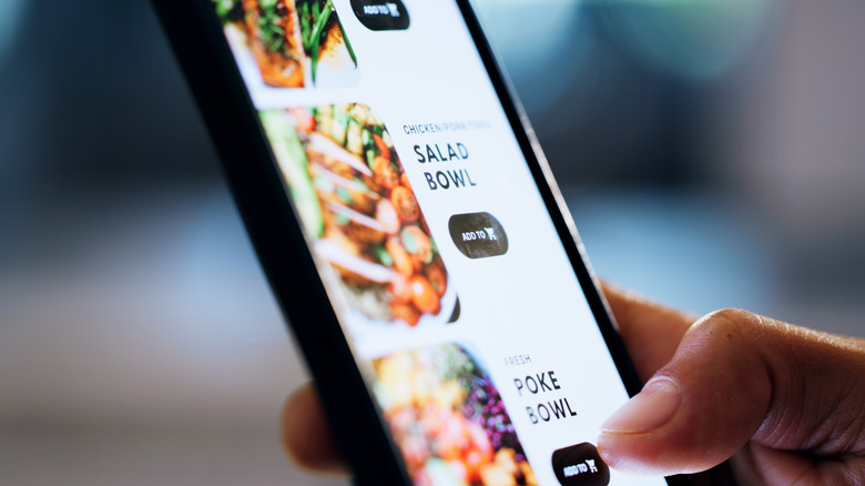 A hand holding a phone showing a menu for a food delivery app