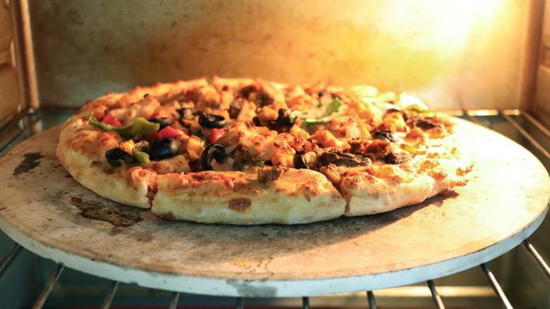 A pizza with puffy crust on a pizza stone in a conventional home oven.