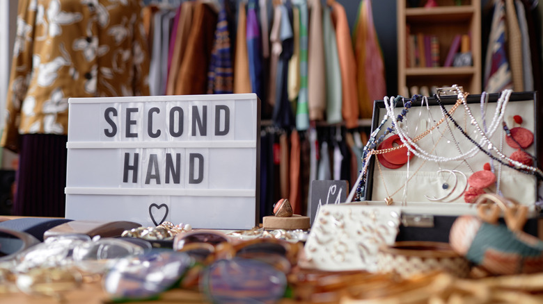 A table at a secondhand store lined with accessories for sale with a clothing rack in the background