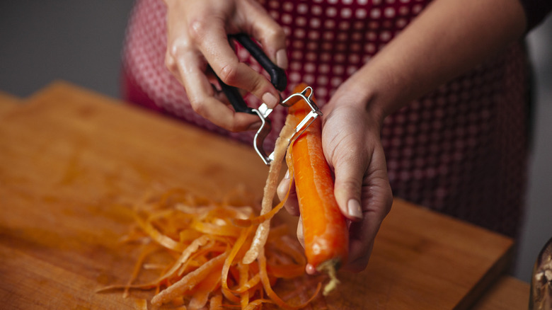 Person peeling a carrot over a wooden cutting board
