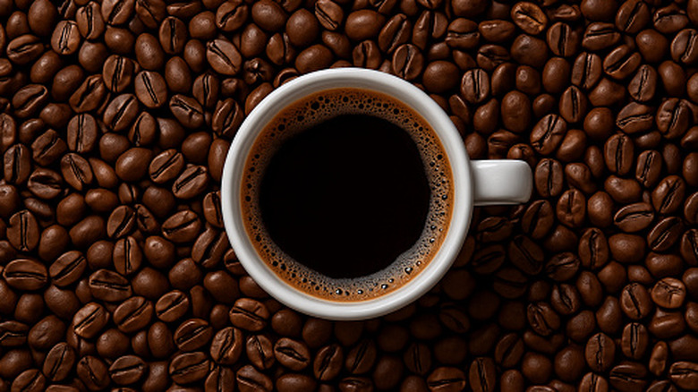 White cup of coffee on background of coffee beans