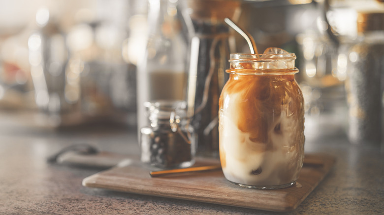 Iced coffee in a mason jar on a wooden cutting board in a home kitchen