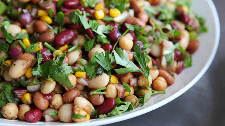 a salad with many types of beans and greens in a white bowl