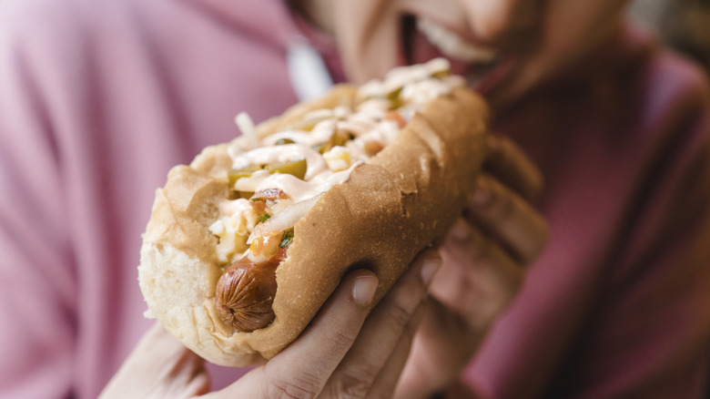 Person about to bite into a large hot dog covered in vegetables