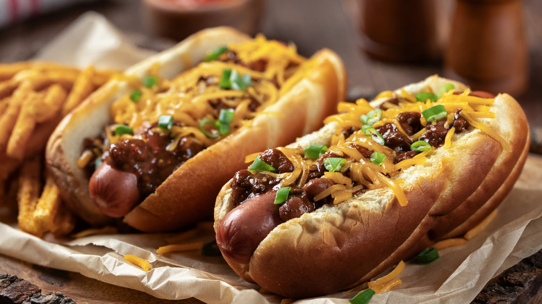 Two hot dogs covered in chili, cheese, and green onions