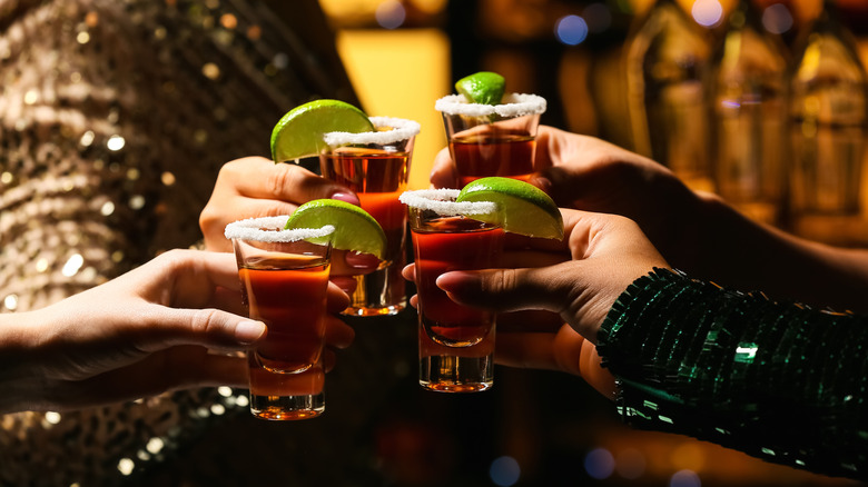 Hands holding tequila shots with salted rims and lime wedges