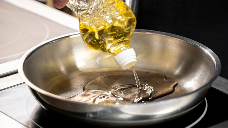 Oil being poured into a stainless steel pan.