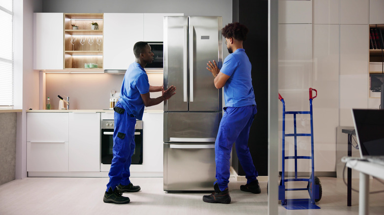 Two delivery persons installing a new fridge