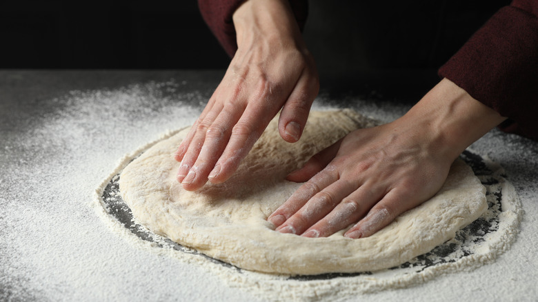 Pizza dough being prepared with hands