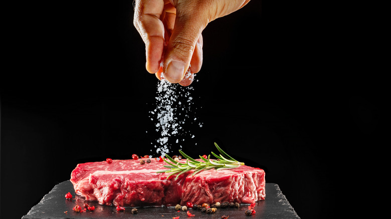 A chef salts a ribeye steak