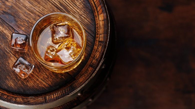 A glass of whiskey on top of a barrel