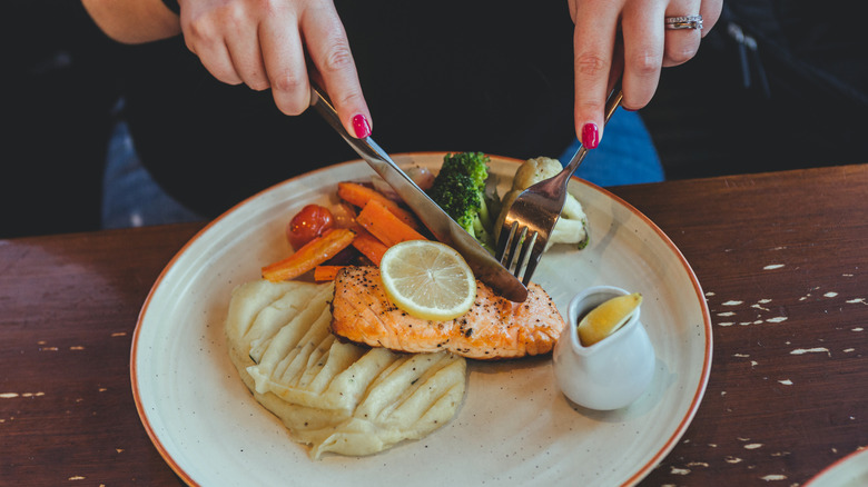 Hands cutting into salmon fillet with knife and fork