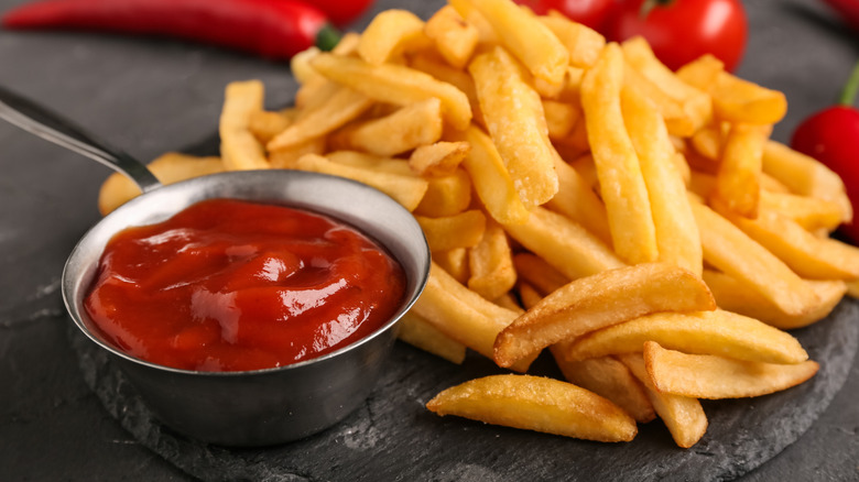 Ramekin of ketchup next to a pile of french fries.