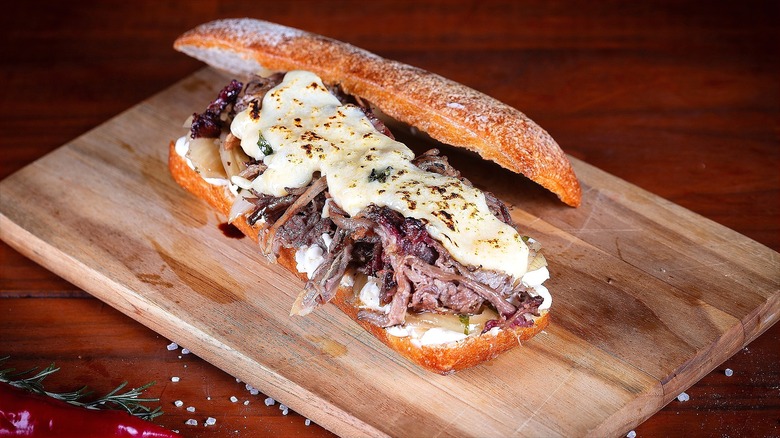 Long toasted roll filled with shredded beef and melted cheese on a wooden cutting board